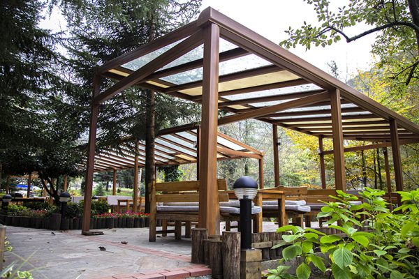 Wood-framed pergola with clear polycarbonate roof and bench seating, highlighting timber as a premium pergola material.