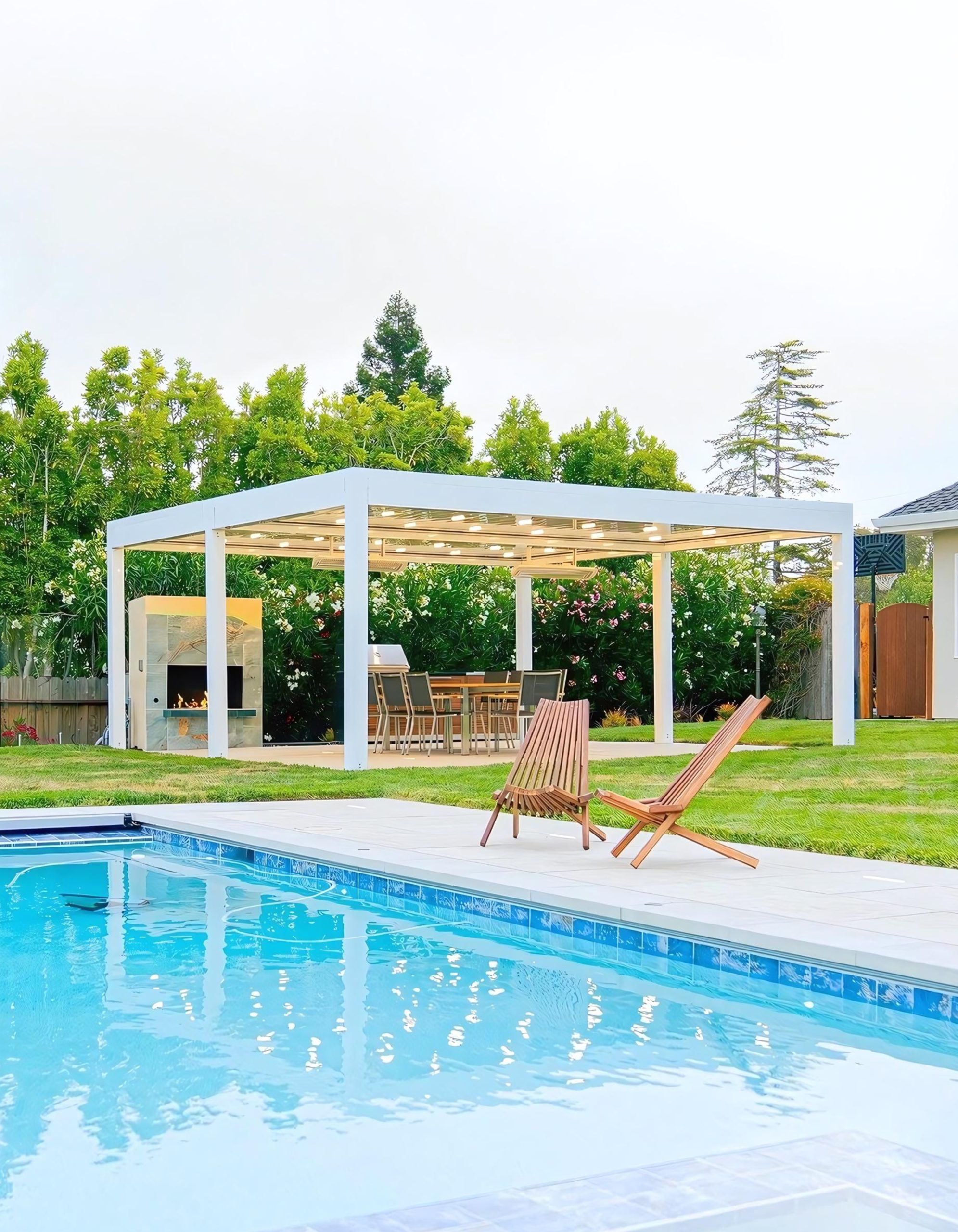 Modern white-frame pergola beyond blue pool, LED-lit slat roof shading dining table and fireplace, plus two wooden loungers.