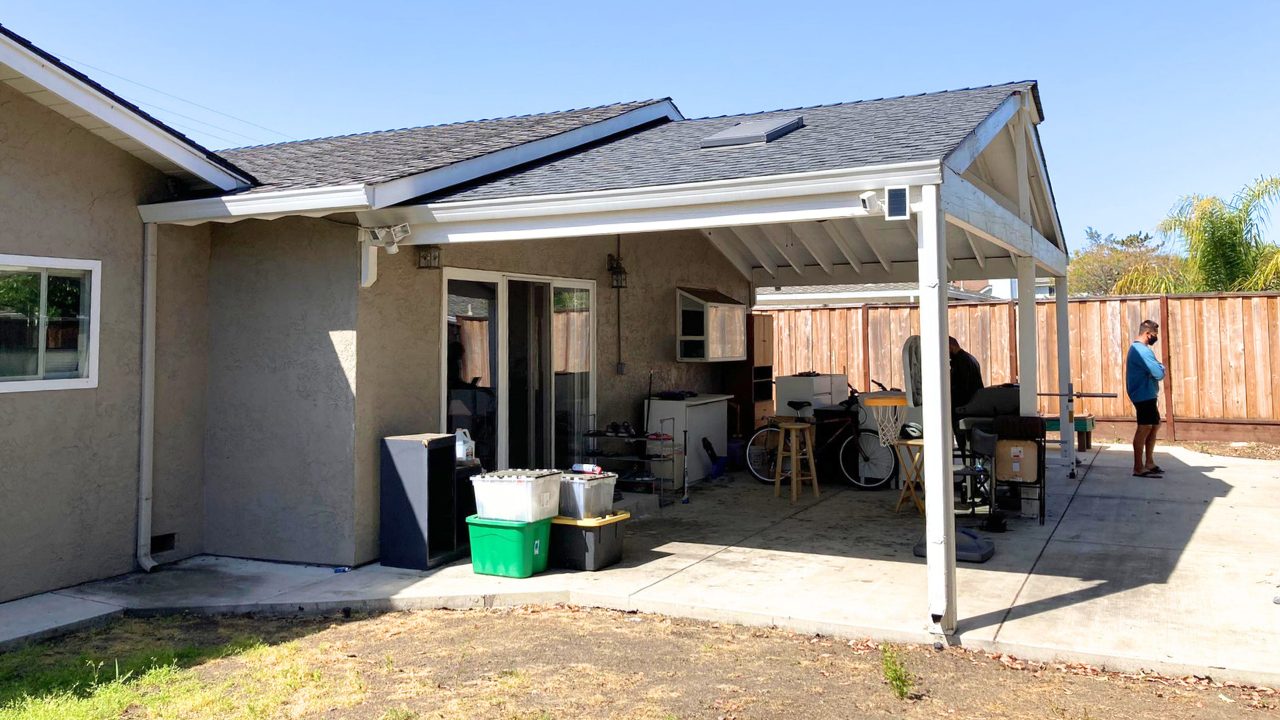 Existing backyard patio with basic gable-roof wood cover and cluttered storage, shown as pre-renovation stage by Pergomatic.