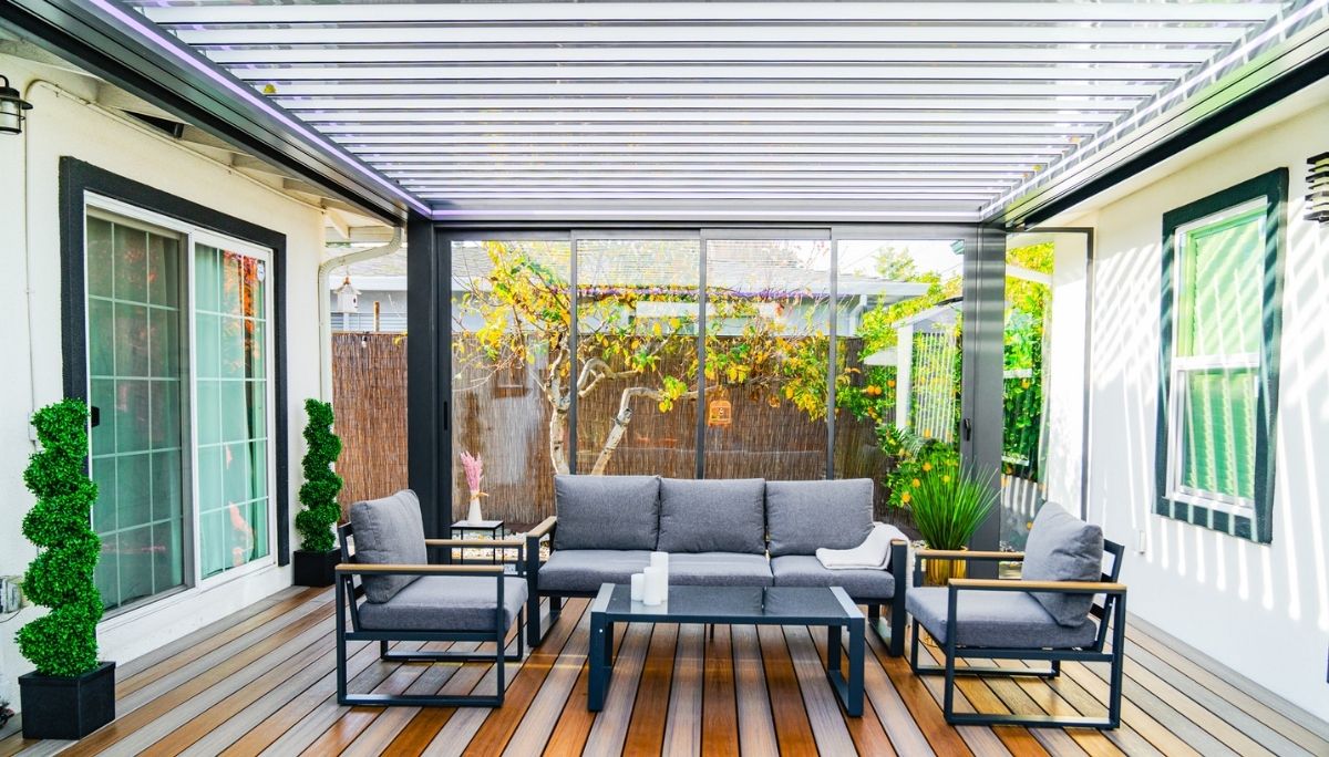 Louvera pergola with open aluminum louvers casts striped light onto wood-deck patio furnished with sleek gray seating.