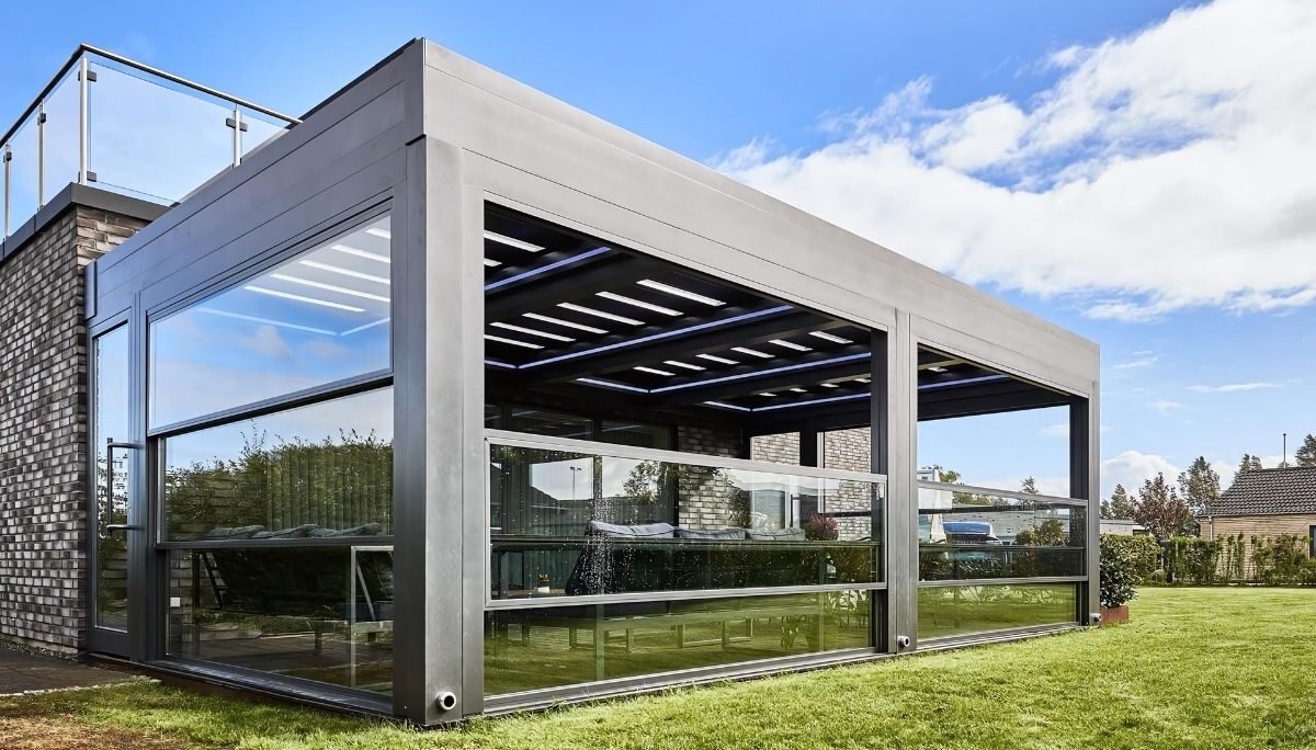 Louvera Glass pergola with sleek grey aluminum frame, retractable glass blades and full-height sliding glass walls on backyard lawn.